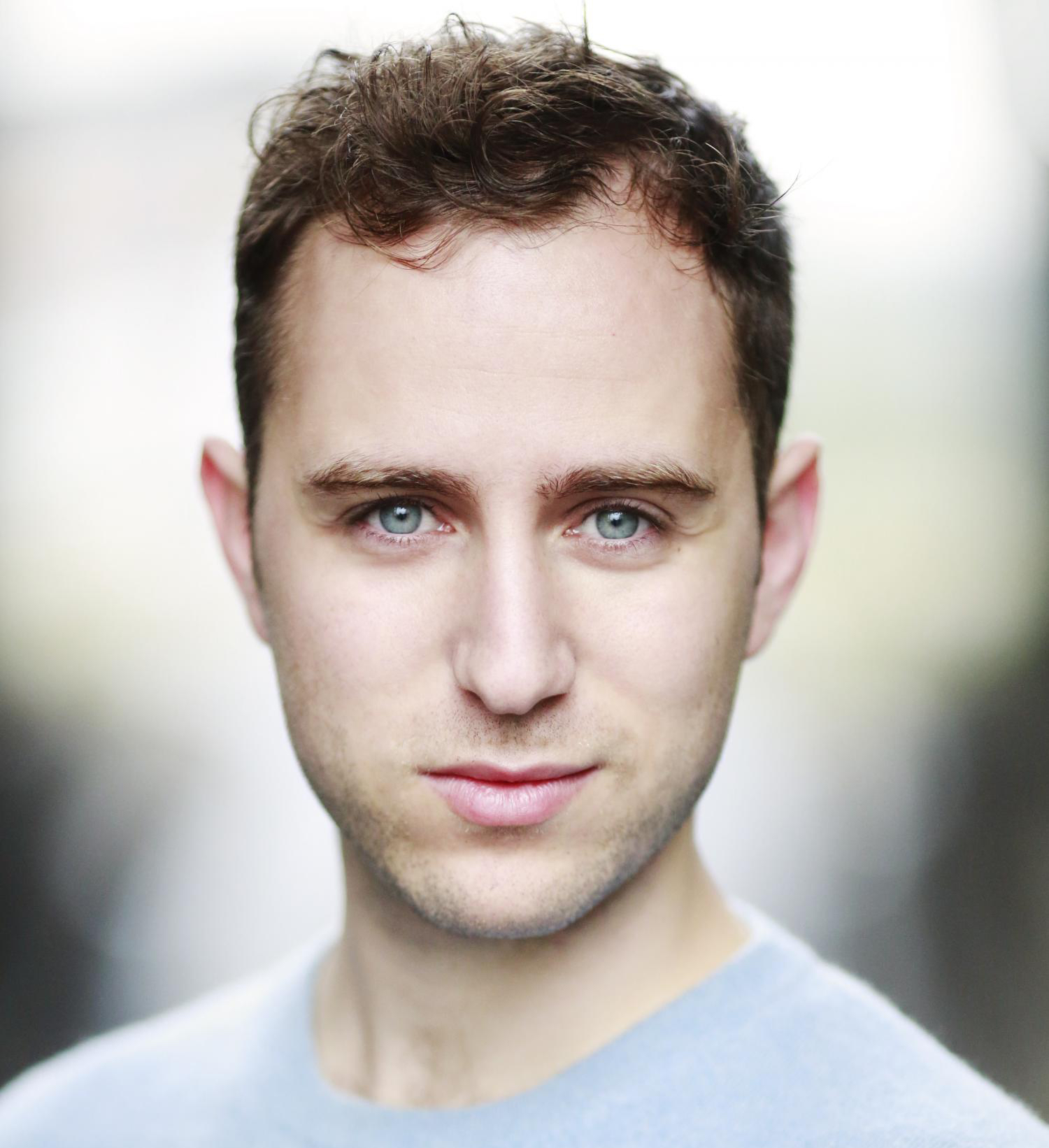 Professional headshot of Guy Woolf, who has blue eyes and wavy brown hair